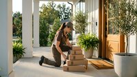 Young woman receiving package delivery at modern home entrance with cardboard boxes and plants in natural sunlight for online shopping concept.