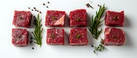 Raw beef tenderloin steaks arranged in two rows with fresh rosemary sprigs, thyme and peppercorns on white background, ready for cooking preparation.