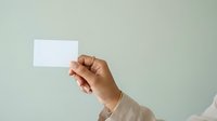 Hand holding blank white business card or namecard against neutral background, suitable for branding, corporate identity, and marketing mockup designs.