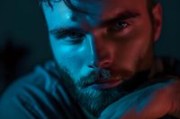 Dramatic close-up portrait of bearded man in contrasting red and blue neon lighting creating mysterious mood and cinematic atmosphere. Dark background adds depth.