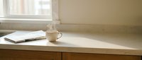 Minimalist wooden kitchen counter with white coffee mug and folded towel near window creating warm morning atmosphere for home interior design.
