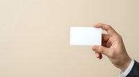 Hand holding blank white business card against neutral beige background, suitable for branding, corporate identity, and marketing mockup designs.