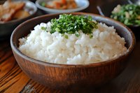 Steamed white rice topped with fresh chopped green onions served in rustic wooden bowl on dark table, traditional Asian cuisine presentation.