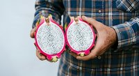 Man in plaid shirt holding halved dragon fruit with white flesh and small black seeds, displaying fresh tropical produce for culinary and healthy eating concepts.