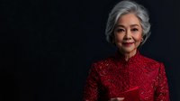 Senior Asian woman in elegant red lace qipao dress smiling warmly against dark background, radiating grace and confidence. Professional portrait highlighting traditional formal attire.