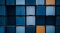 Stacked shipping containers creating geometric pattern in shades of blue and orange, industrial cargo storage background for transportation and logistics concepts.