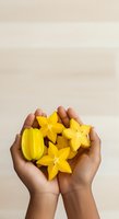 Hand holding fresh yellow star fruit and carambola slices against neutral background, showcasing tropical fruit for food, nutrition, healthy eating, and culinary design projects.