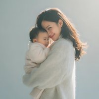 Young Asian mother in cream sweater tenderly holding newborn baby, bonding moment with soft natural lighting for family and parenting concepts.
