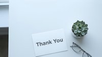 Thank you card on white desk with succulent plant and glasses, minimal flat lay composition for gratitude, appreciation, and business concepts.