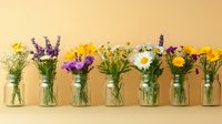 Colorful wildflowers in glass jars arranged in a row against a warm beige background, featuring daisies, lavender, and yellow blooms.