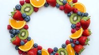 Fresh fruit wreath with strawberries, blueberries, kiwi, oranges and raspberries arranged in circle on white background for healthy eating concepts.