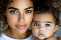 Close up portrait of young mother and toddler with curly hair and striking blue eyes showing tender family moment and natural beauty against light background.