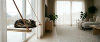 Cozy tabby cat relaxing on wooden hanging shelf by window in modern minimalist living room with natural light and houseplants.