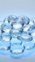 Transparent blue gel capsules or water beads piled together on a reflective surface, showcasing a glossy, hydrating aesthetic for beauty and wellness concepts.
