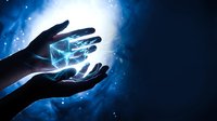 Hands holding glowing digital cube with blue light effects and particles on dark background for technology and innovation concepts.