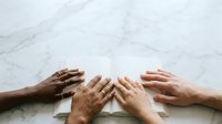 Diverse group of people stacking hands together on marble surface, symbolizing teamwork, unity, collaboration, and shared commitment to common goals.
