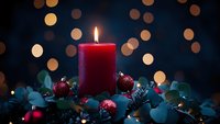 Red candle burning with Christmas ornaments and eucalyptus leaves against dark background with warm bokeh lights for holiday decoration and festive atmosphere.