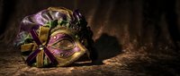 Ornate carnival mask with golden details and purple ribbons resting on textured surface against dark moody background for masquerade events and celebrations.