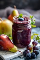 Fresh homemade grape and pear jam in glass jar garnished with blueberry and mint leaves, surrounded by fresh fruits on rustic wooden surface in moody lighting.