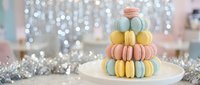 Colorful French macarons arranged in elegant pyramid on white plate with sparkling bokeh lights and silver tinsel creating festive holiday atmosphere.