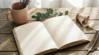 Open blank notebook with empty pages on rustic wooden table with eucalyptus branch, coffee mug and natural lighting for journaling and writing projects.