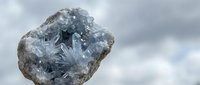 Raw celestite crystal specimen with blue formations against cloudy sky background for geology education and mineral collection displays.