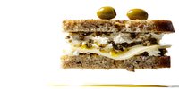 Gourmet sandwich with layers of cheese, meat, and green olives on multigrain bread, isolated on white background for food photography and menu design.