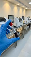 Medical technician in blue gloves holding blood sample tube with barcode in modern laboratory with automated equipment for clinical testing and analysis.
