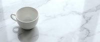 Empty white ceramic cup with handles on marble surface with veining, isolated on white background, suitable for product mockups, branding, and design projects.
