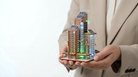 Professional businesswoman in beige suit holding miniature eco-friendly city model with solar panels and green buildings for sustainable development presentation.