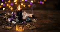 Mystical tarot reading setup with burning candles, crystals, and cards on wooden table with colorful bokeh lights creating magical atmosphere for divination.