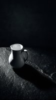 Black and white ceramic pitcher with handle on dark textured surface, casting dramatic shadow. Minimalist still life composition for home decor, kitchenware marketing, and artistic projects.
