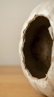 Close-up of handmade ceramic pottery vessel with organic opening on wooden surface showcasing artisan craftsmanship and natural clay texture.
