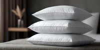 Stack of three white fluffy pillows on bed in modern bedroom interior for comfortable sleep and home decor.