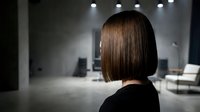 Woman with straight brown bob haircut viewed from behind in modern minimalist interior space with ambient lighting.