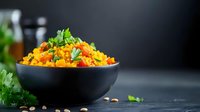 Colorful vegetarian rice pilaf with vegetables and herbs served in black bowl on dark slate background for healthy cooking and dining concepts.