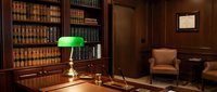 Classic lawyer office interior with wooden desk, green banker lamp, leather chair and bookshelf filled with legal books for professional workspace design.