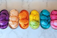 Colorful scoops of artisanal gelato in vibrant rainbow colors arranged in oval dishes on marble background, showcasing diverse flavors and smooth textures.