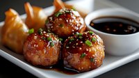 Glazed Asian meatballs with soy dipping sauce garnished with sesame seeds and green onions, served with crispy wontons on white ceramic plate.