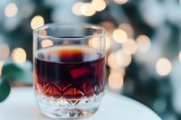 Glass of red mulled wine or cocktail on white surface against blurred bokeh lights background, festive winter drink with crystal pattern detail.