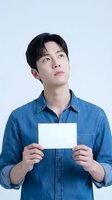 Young Asian male wearing denim shirt holding blank white card against neutral background, suitable for advertising, marketing campaigns, and promotional materials.