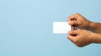 Close-up of male hands with medium skin tone holding blank white business card against light blue background for branding and corporate identity mockups.