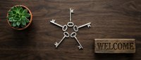 Vintage silver keys arranged in a star pattern on a wooden surface with a succulent plant and a rustic welcome sign, symbolizing home ownership.