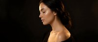 Young brunette woman in profile with elegant updo hairstyle and golden lighting against dark background for beauty and fashion concepts.
