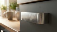 Modern stainless steel kitchen cabinet handle on gray cabinetry with wooden countertop and ceramic bowls in blurred background for interior design.