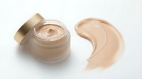 Luxury foundation cream in glass jar with golden cap and makeup smear on white background. Premium cosmetic product for skincare and beauty routine.