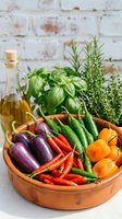 Colorful fresh vegetables in a rustic clay bowl with olive oil and herbs, featuring eggplants, red and green chili peppers, and yellow peppers.