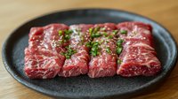Fresh raw marbled beef slices arranged on dark plate with herbs, premium quality meat cuts ready for grilling or cooking in restaurant kitchen setting.