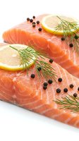 Fresh salmon fillets garnished with lemon slices, dill and black peppercorns on white background, ready for cooking healthy seafood dinner or gourmet meal preparation.