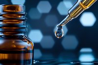 Dropper bottle with essential oil or medical liquid against blue bokeh background, close-up macro shot showing transparent drop falling from glass pipette.
